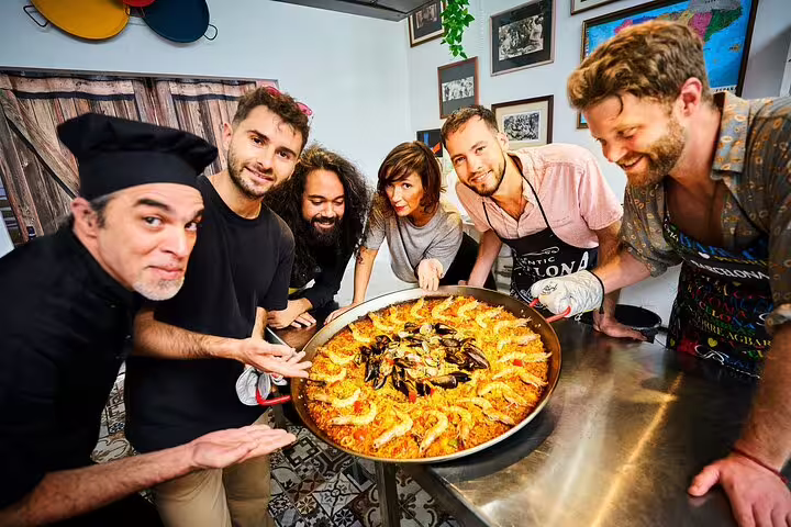 Group of enthusiastic participants showcasing a large, freshly cooked paella during the Ultimate Paella Cooking Class Experience.