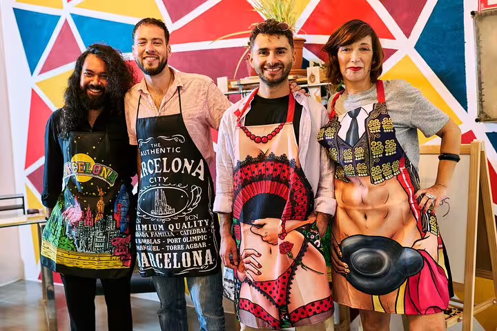 Four smiling participants wearing colorful aprons at a vibrant paella cooking class in Barcelona, showcasing culinary fun.