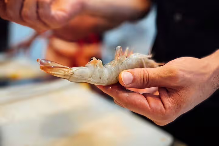 Hands expertly holding fresh shrimp during the Ultimate Paella Cooking Class Experience, highlighting seafood preparation skills.