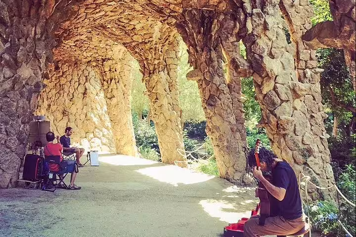 Visitors enjoy a live guitar performance under the stone arches of Park Güell during a Barcelona private tour with tapas.