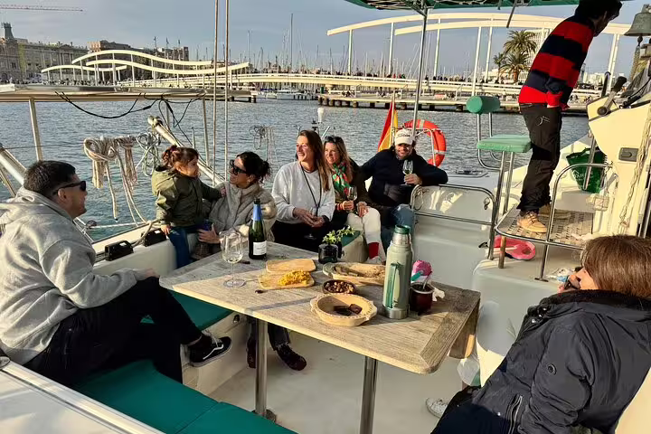 Group enjoying snacks and cava on a private catamaran tour in Barcelona, with a view of the marina and city skyline.