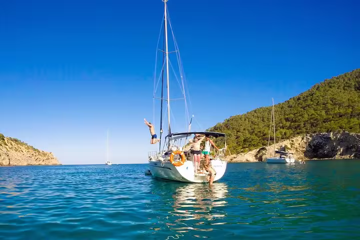 Family enjoying a private sailing tour in Barcelona, diving into clear waters with scenic views and drinks on a sunny day.