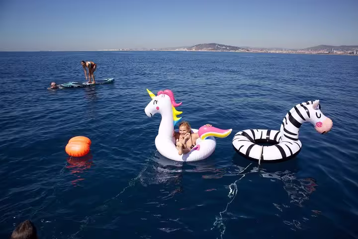 Family enjoying a Barcelona private sailing tour with drinks, featuring vibrant inflatable floats on the sparkling Mediterranean Sea.