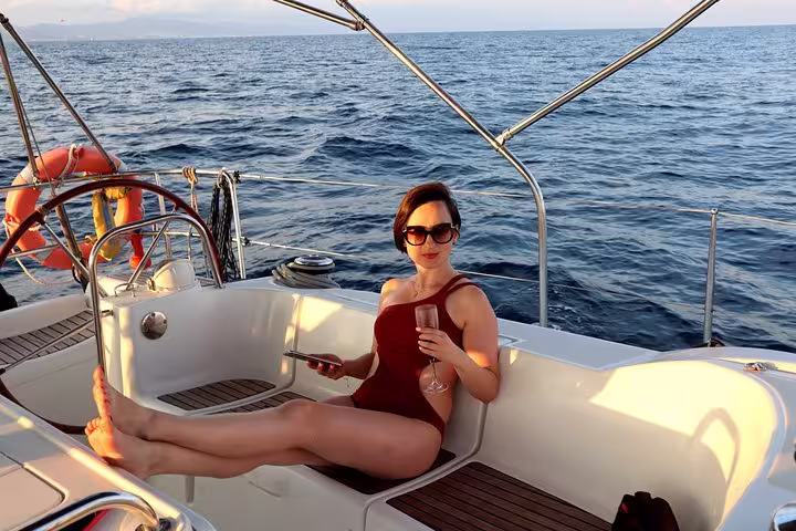 A woman relaxes with a drink on a private sailing tour in Barcelona, enjoying the sun and sea views on a luxury yacht.