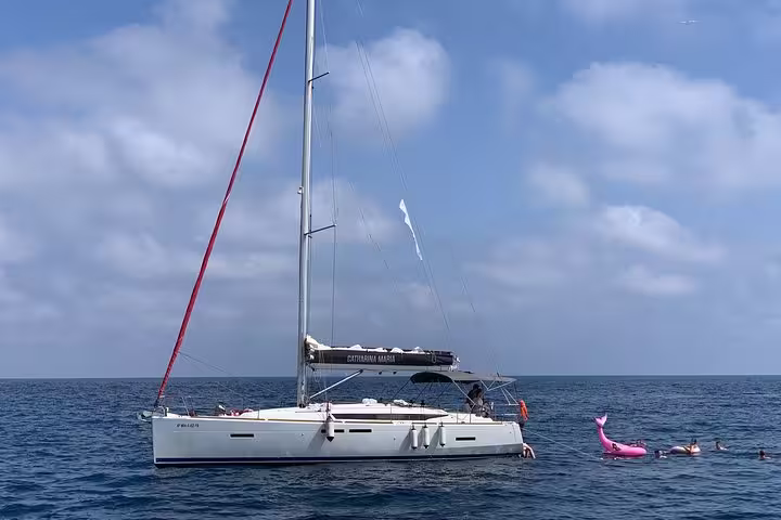 Sailboat anchored in the Mediterranean Sea during a Barcelona private sailing tour, with people swimming and enjoying drinks.
