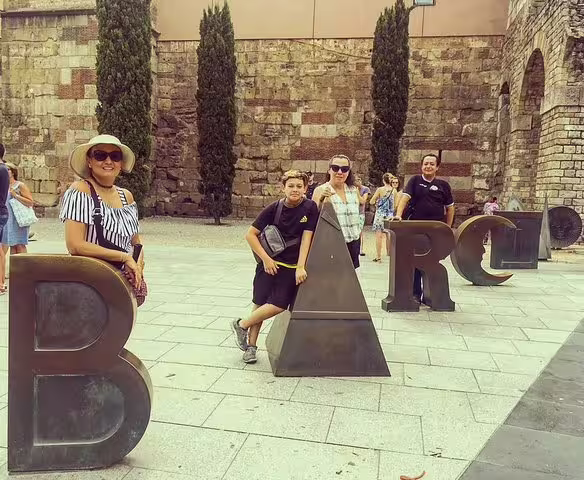 Tourists enjoy a private tour in Barcelona, posing with iconic letter sculptures, showcasing city highlights and secrets.