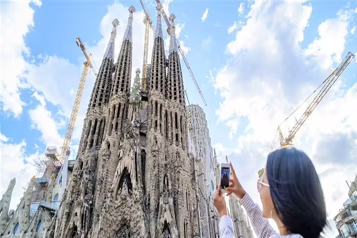 Tourist captures the iconic Sagrada Familia spires against a bright sky, highlighting Barcelona's architectural marvel.