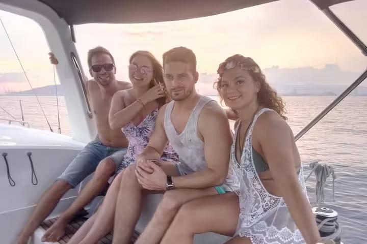 Friends relaxing on a Barcelona sailing tour at sunset, enjoying open bar drinks and onboard snacks