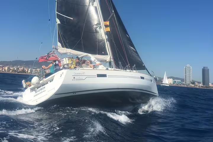 Sailboat gliding through Barcelona's blue waters during a 3-hour exclusive trip with tapas and drinks, city skyline in view.