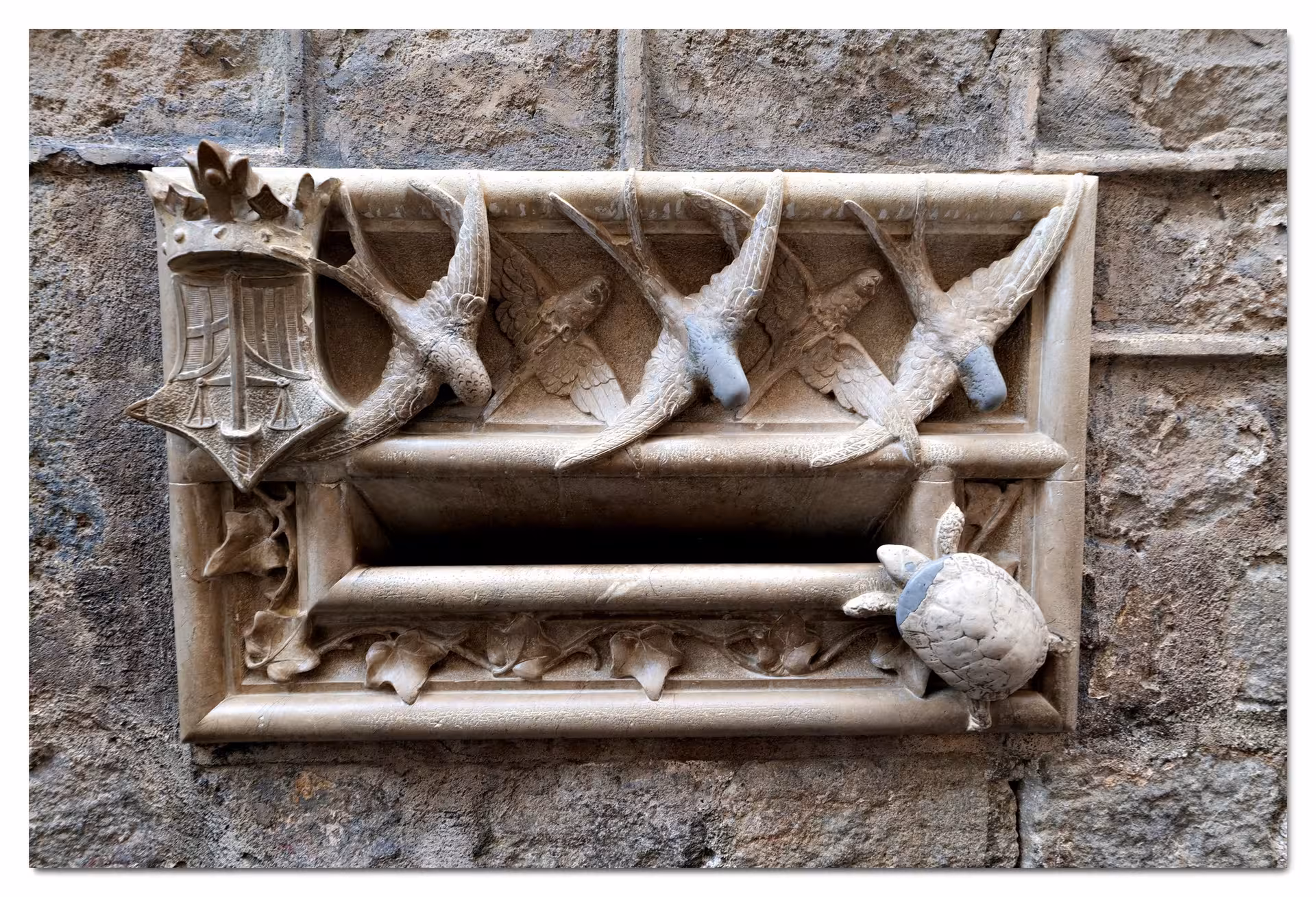 Intricate stone carving of swallows and a turtle on Barcelona's historic wall, embodying city legends.