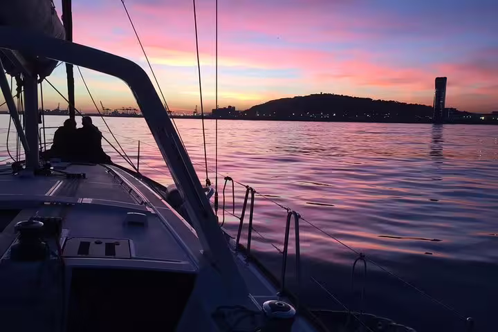Sailboat gliding on calm waters during a vibrant Barcelona sunset cruise, highlighting the city skyline and colorful sky.