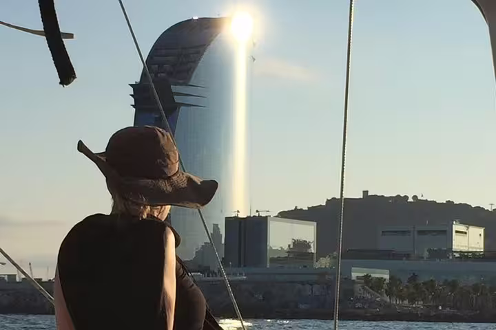 Woman in a sun hat enjoys a stunning Barcelona sunset view from a yacht, with the iconic city skyline in the background.
