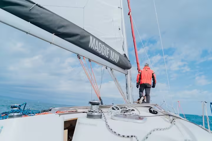 Person in red jacket walking on a sailboat deck under clear skies, offering a serene Barcelona sunset sailing experience.