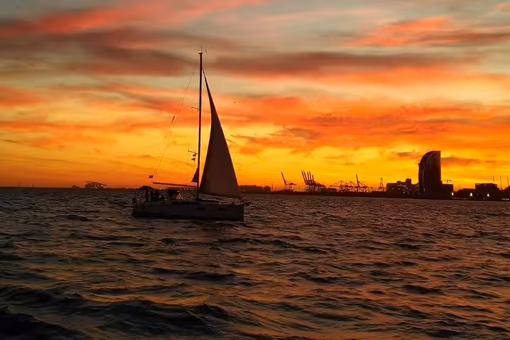 Sailboat cruising at golden sunset near Barcelona skyline, private sailing experience with open bar and snacks