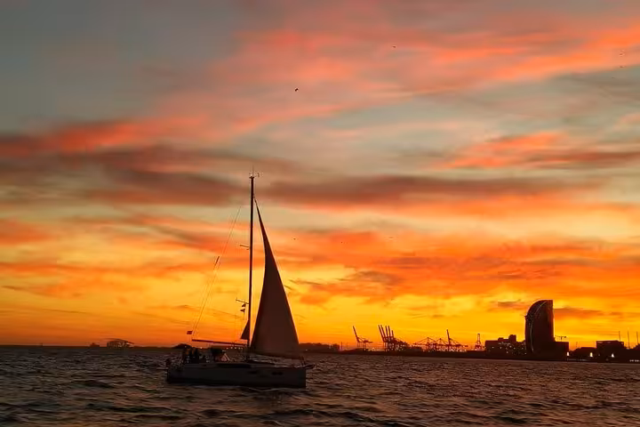 Sailboat cruising off Barcelona at golden sunset, ideal for private sailing tour with live saxophone and open bar