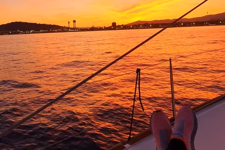 Barcelona sunset private sailing view from yacht deck, glowing sea horizon, open bar cruise experience