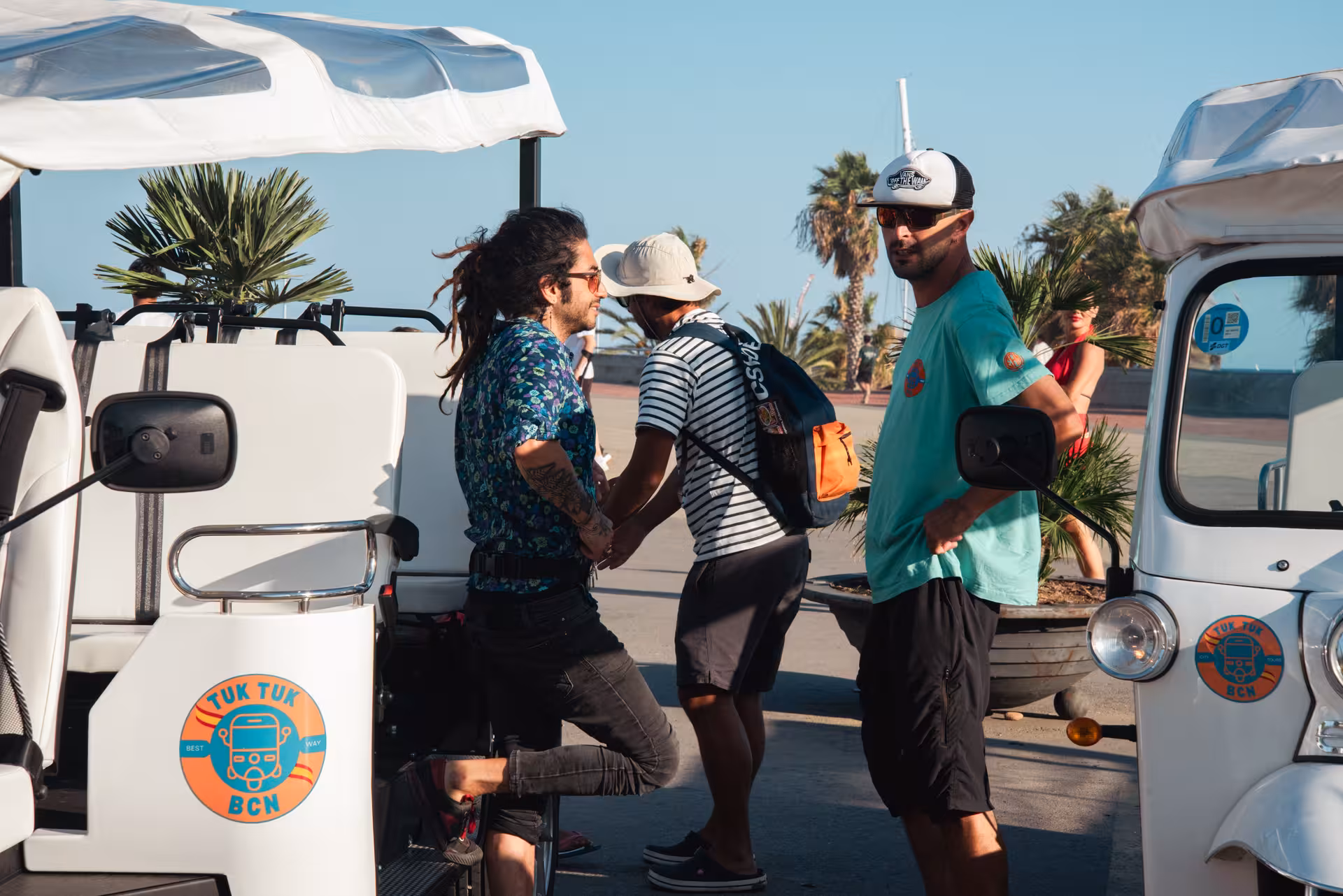 Guests meet their guide beside a Barcelona tuk tuk on the seaside promenade before the city highlights tour