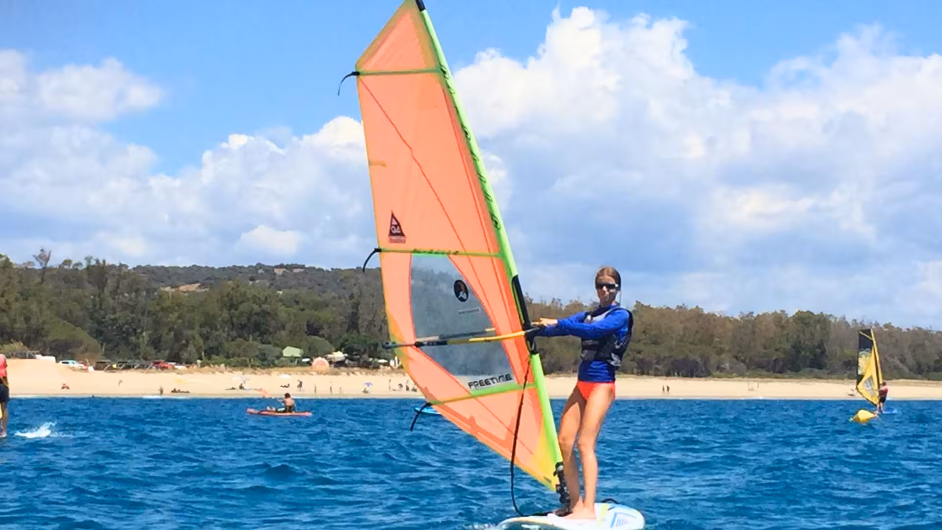 Windsurfing enthusiast navigates the sparkling waters of Bari Sardo during a basic windsurf course under sunny skies.