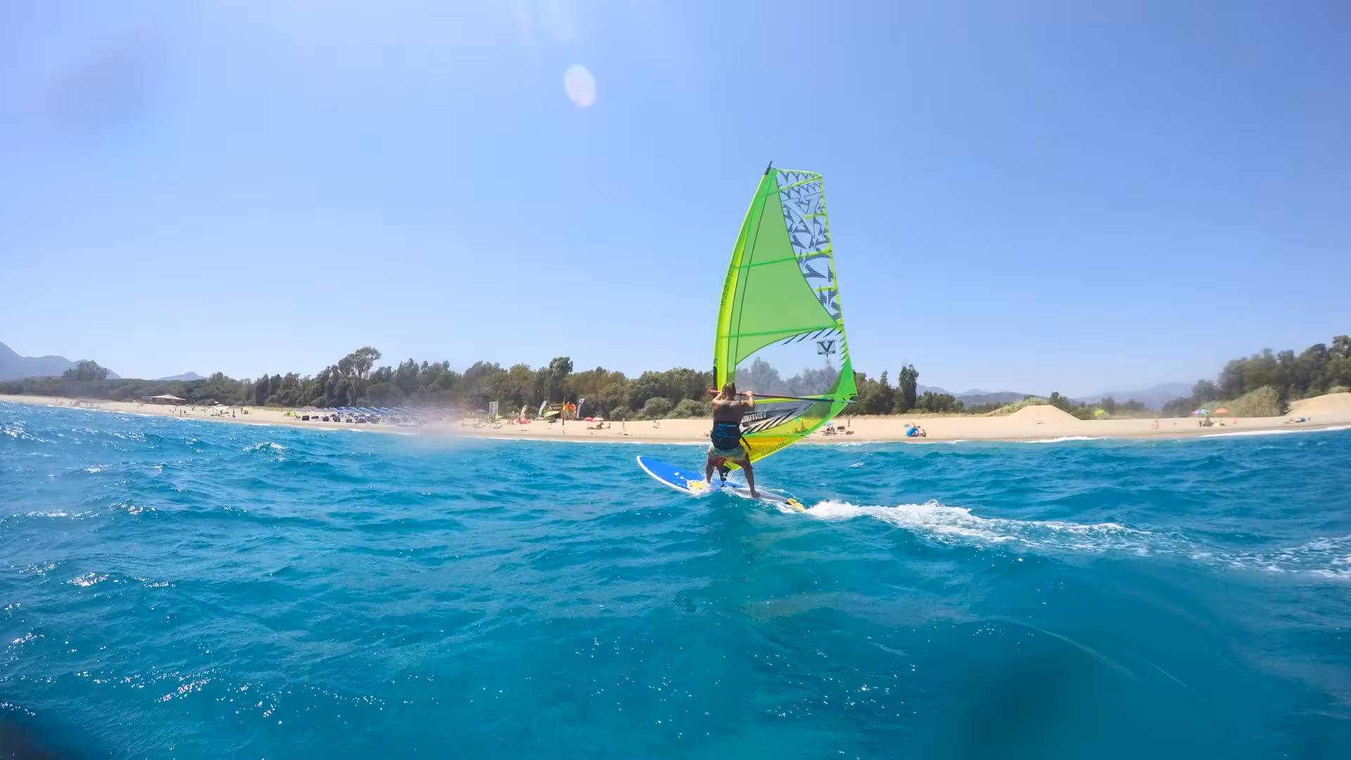Windsurfer gliding over turquoise waves in Bari Sardo, perfect location for a basic windsurf course under clear skies.