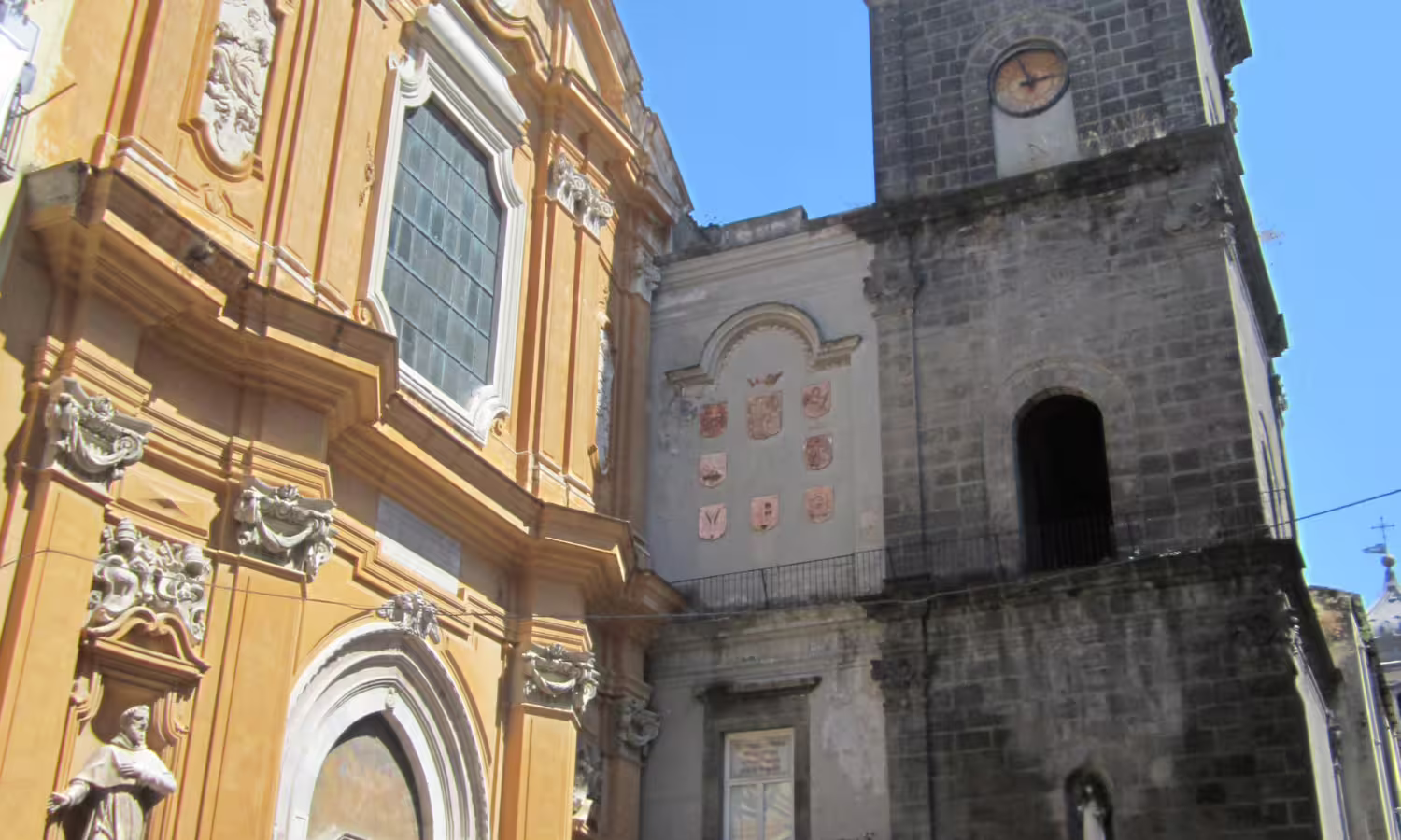 Baroque church facade and stone bell tower under blue sky in Naples historic center on a guided 2‑day sightseeing tour