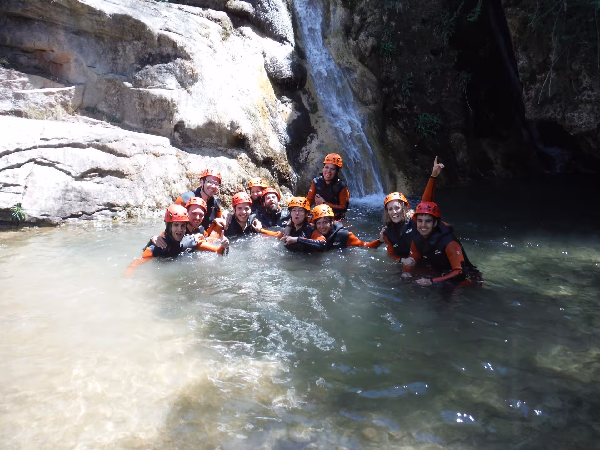 Grupo con casco y neopreno en poza bajo cascada, barranco acuático en Riodeva, Teruel, aventura guiada