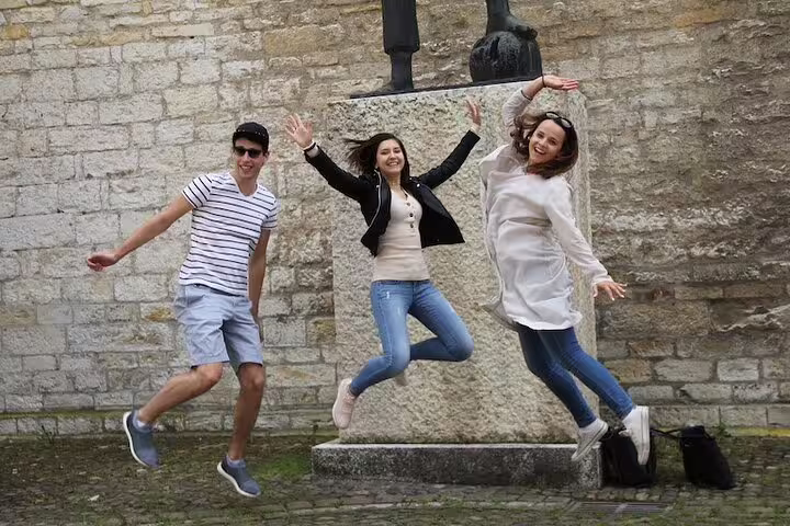 Friends jump by a stone monument in Basel Old Town during a self-guided scavenger hunt sightseeing tour