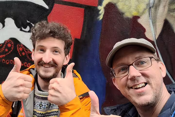 Two travelers give thumbs up by colorful street art on a Basel self-guided scavenger hunt and sights tour