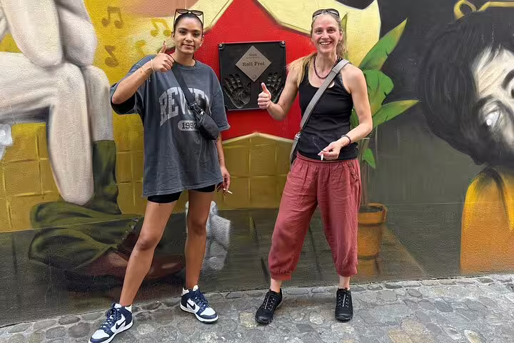 Two travelers give thumbs up by a Basel mural landmark on a self-guided scavenger hunt and city sights tour