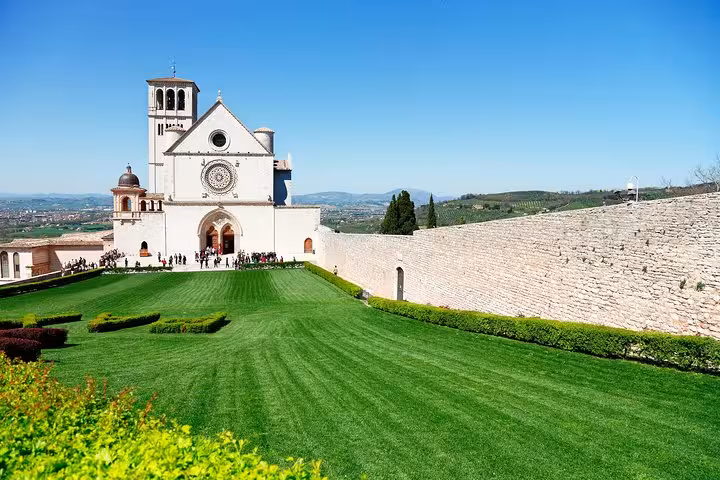 Stunning view of the Basilica of Saint Francis in Assisi with vibrant green lawns and a clear blue sky.