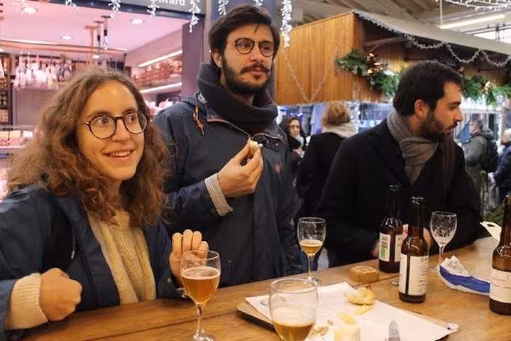 Visitors enjoying drinks and snacks inside a bustling Parisian market during the Bastille & Paris Best Market Food Tour.