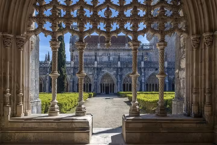 View through ornate arches into the peaceful cloisters of Batalha Monastery, showcasing gothic architecture and gardens.