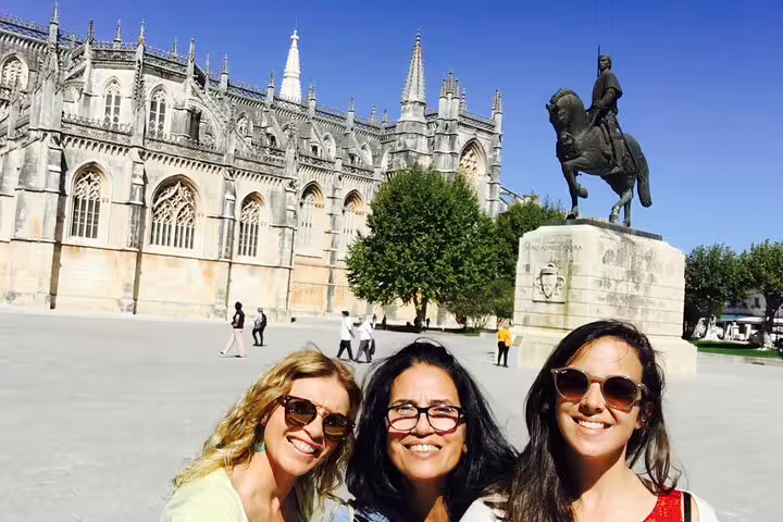 Visitors enjoy a sunny day at Batalha Monastery with a historic statue, part of the guided Fatima, Batalha, Nazaré, and Obidos tour.