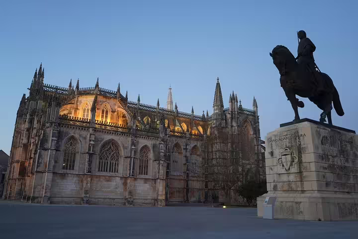 Illuminated Batalha Monastery with equestrian statue at dusk, highlighting Gothic architecture on the Óbidos to Fatima tour.