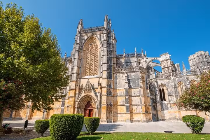 Exterior view of Batalha Monastery's gothic architecture, featuring intricate stonework under a clear blue sky.