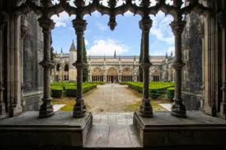 View through ornate columns at Batalha Monastery, highlighting the detailed Gothic stonework and lush central courtyard.