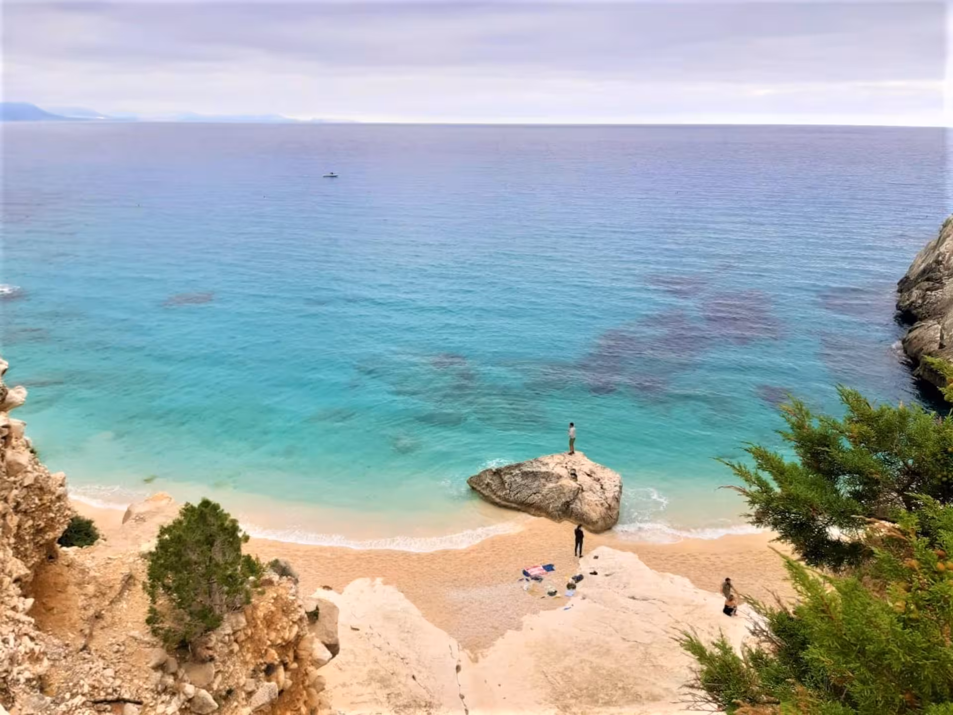 Serene scene at Cala Goloritzè, featuring clear blue waters, sandy beach, and scenic rock formations for trekking.