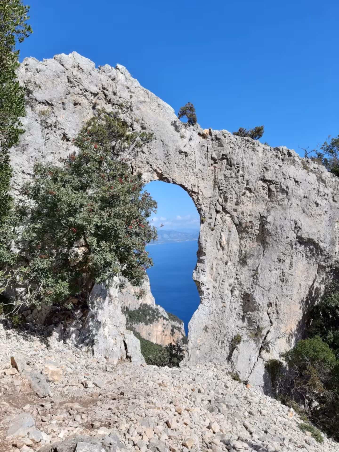 Stunning sea view framed by a natural rock arch on the Baunei trail to Cala Mariolu, under a clear blue sky.