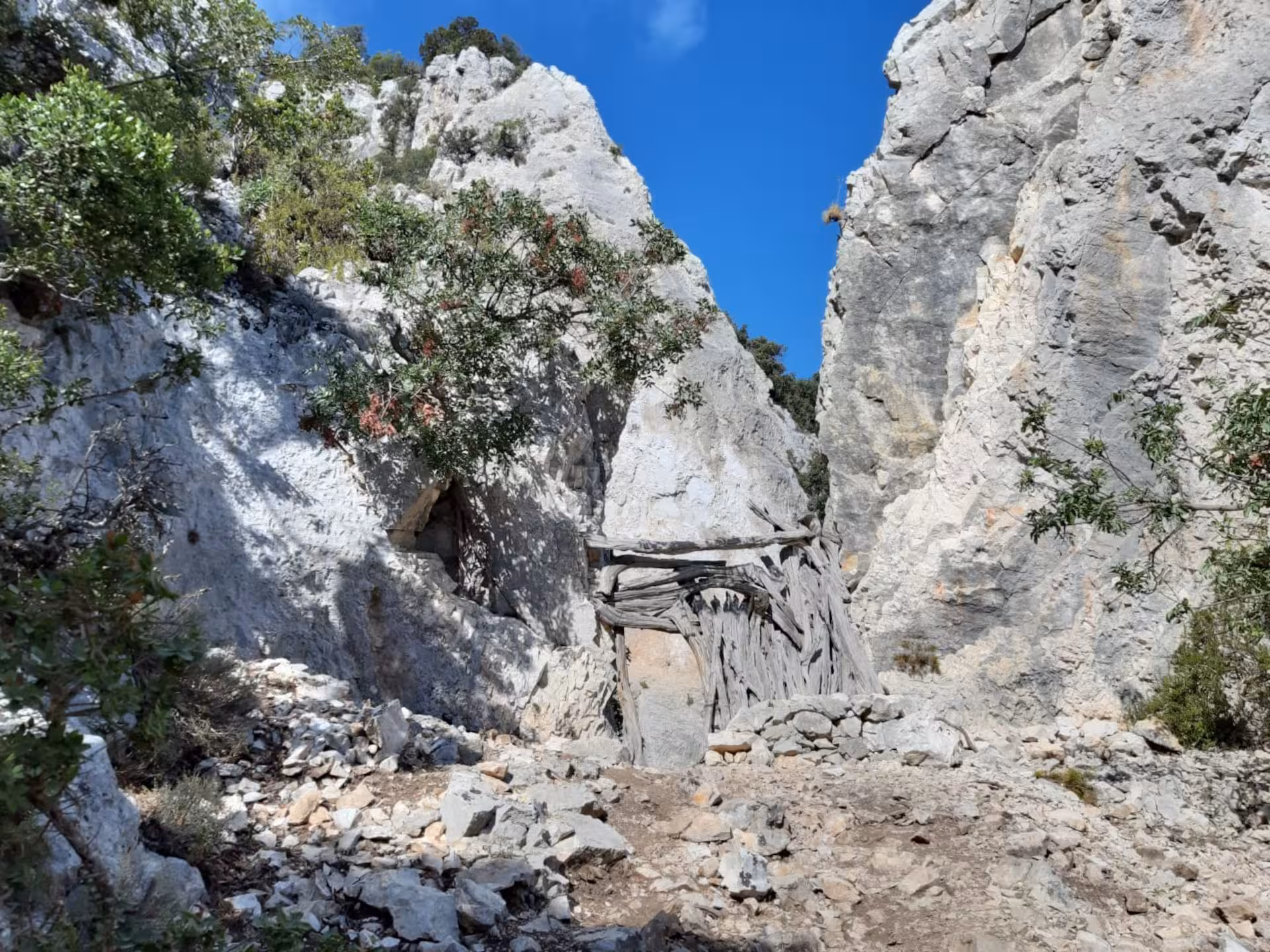 Narrow rocky passage with rustic wooden structure on the Baunei trail to Cala Mariolu.