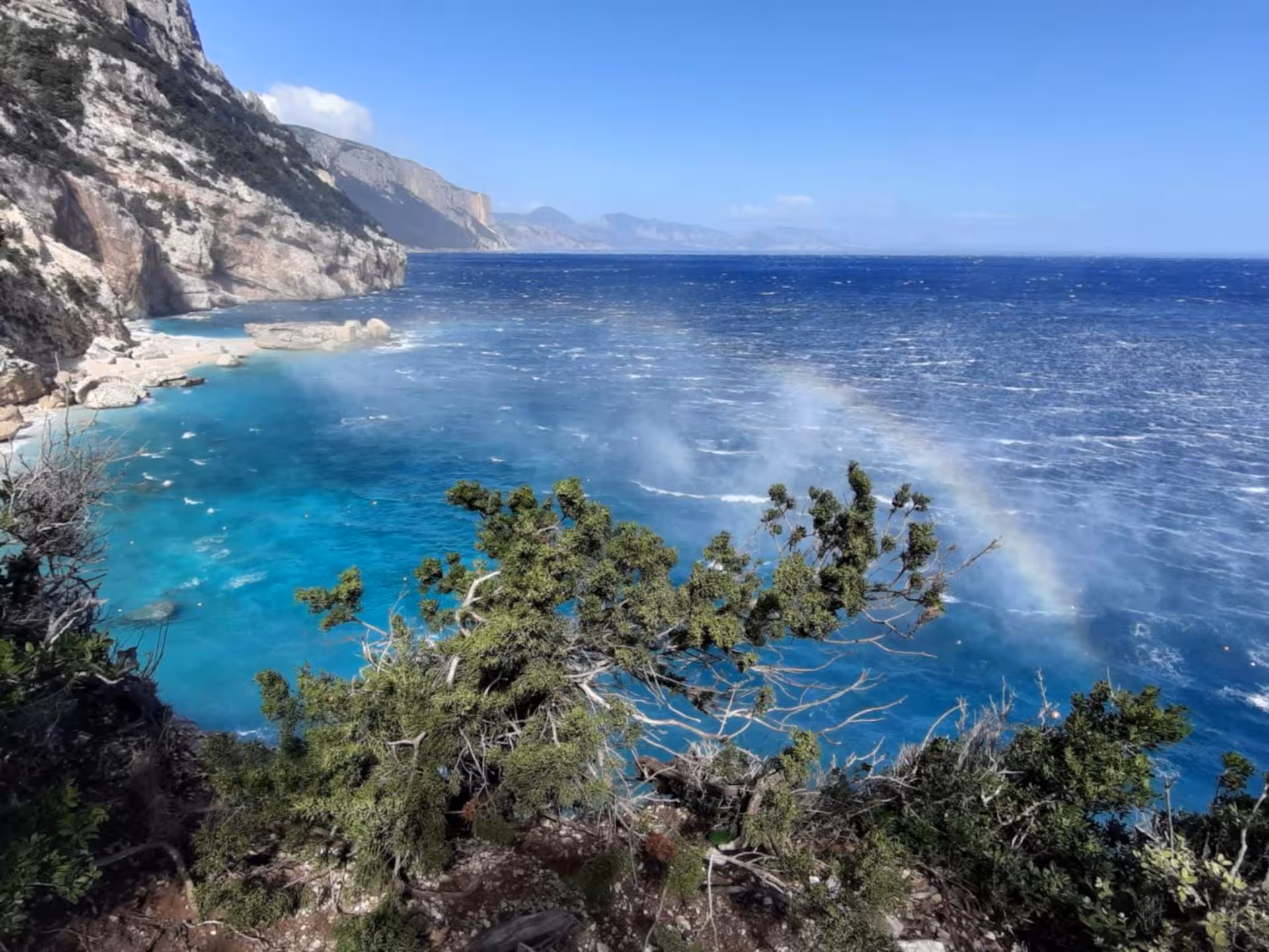 Stunning view of turquoise waters and cliffs with a rainbow at Cala Mariolu in Baunei, Sardinia.