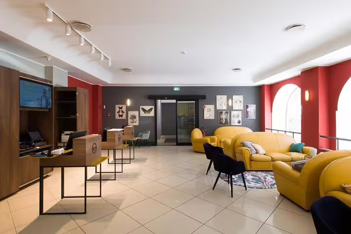 Bright lobby of B&B Hotels Palermo Quattro Canti with yellow sofas and check-in desks, ideal for Palermo Airport transfer stays