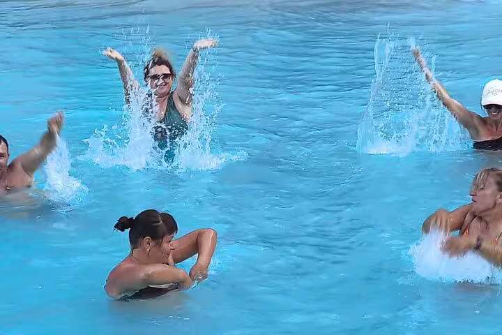 Group enjoying lively aqua activities in a clear blue swimming pool, perfect for a refreshing break on a sunny beach day.