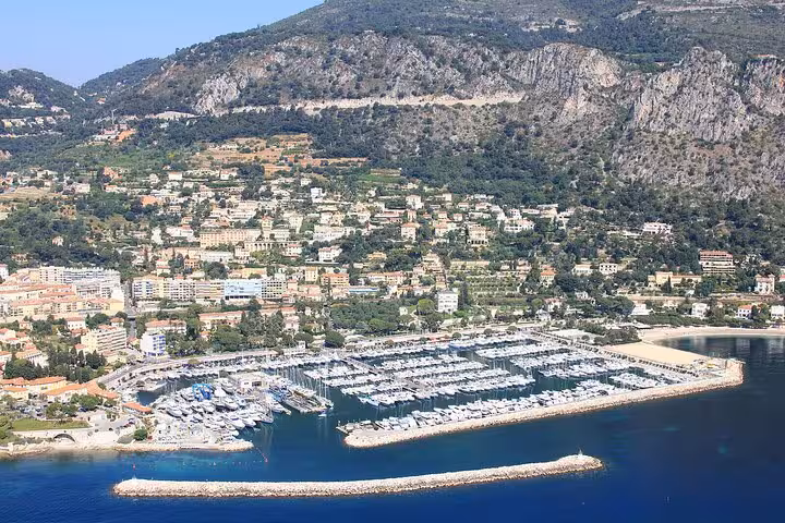 Panoramic view of Beaulieu-sur-Mer marina with boats docked against the backdrop of lush hills and coastline.