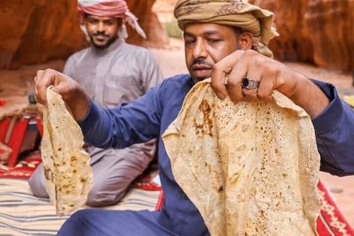 Bedouin host serving fresh flatbread at desert camp dinner on Super Safari quads and camel ride from Sharm