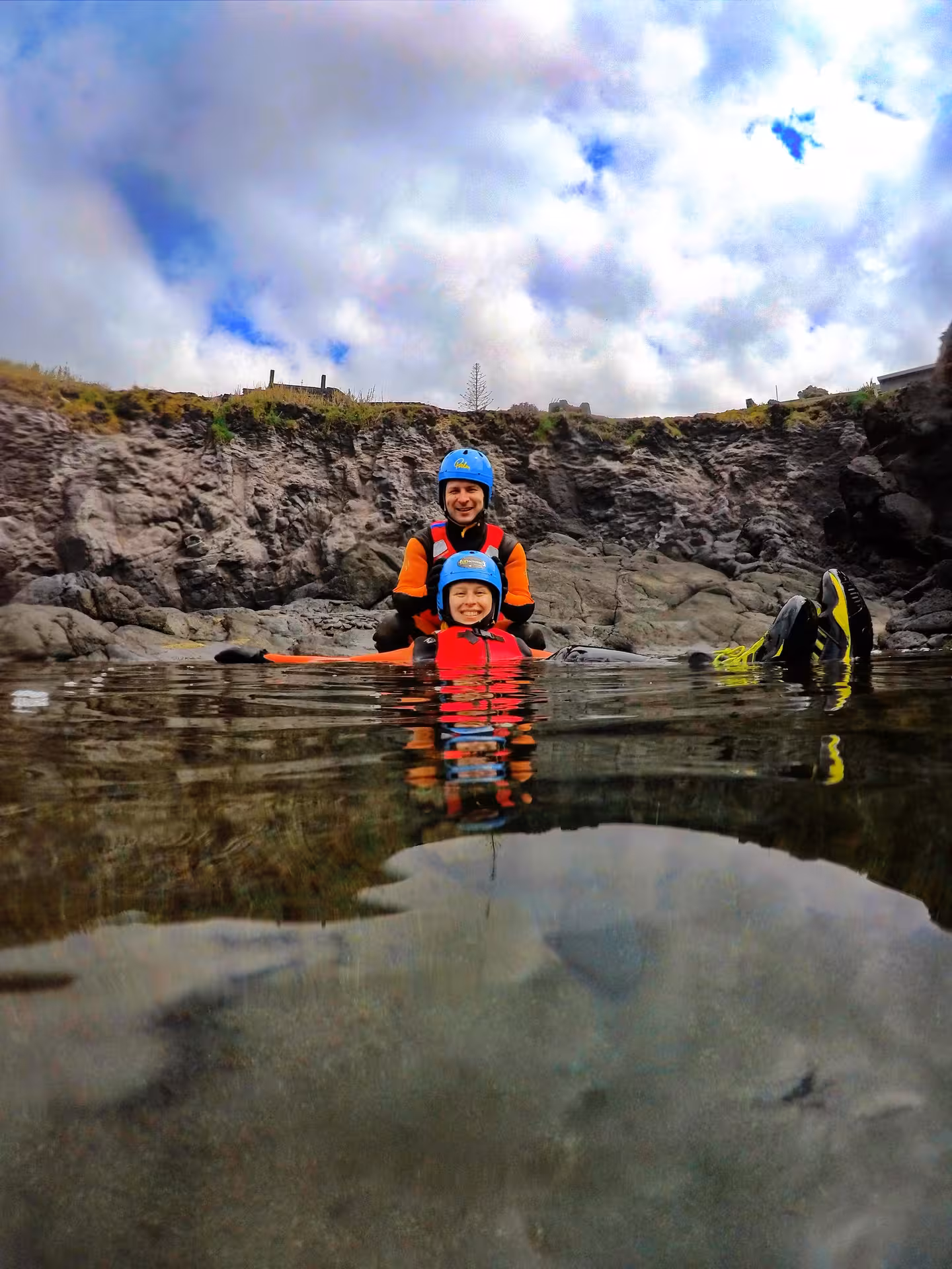 Beginner coasteering Freshman tour, guide and child in helmets floating in calm sea by rocky cliffs