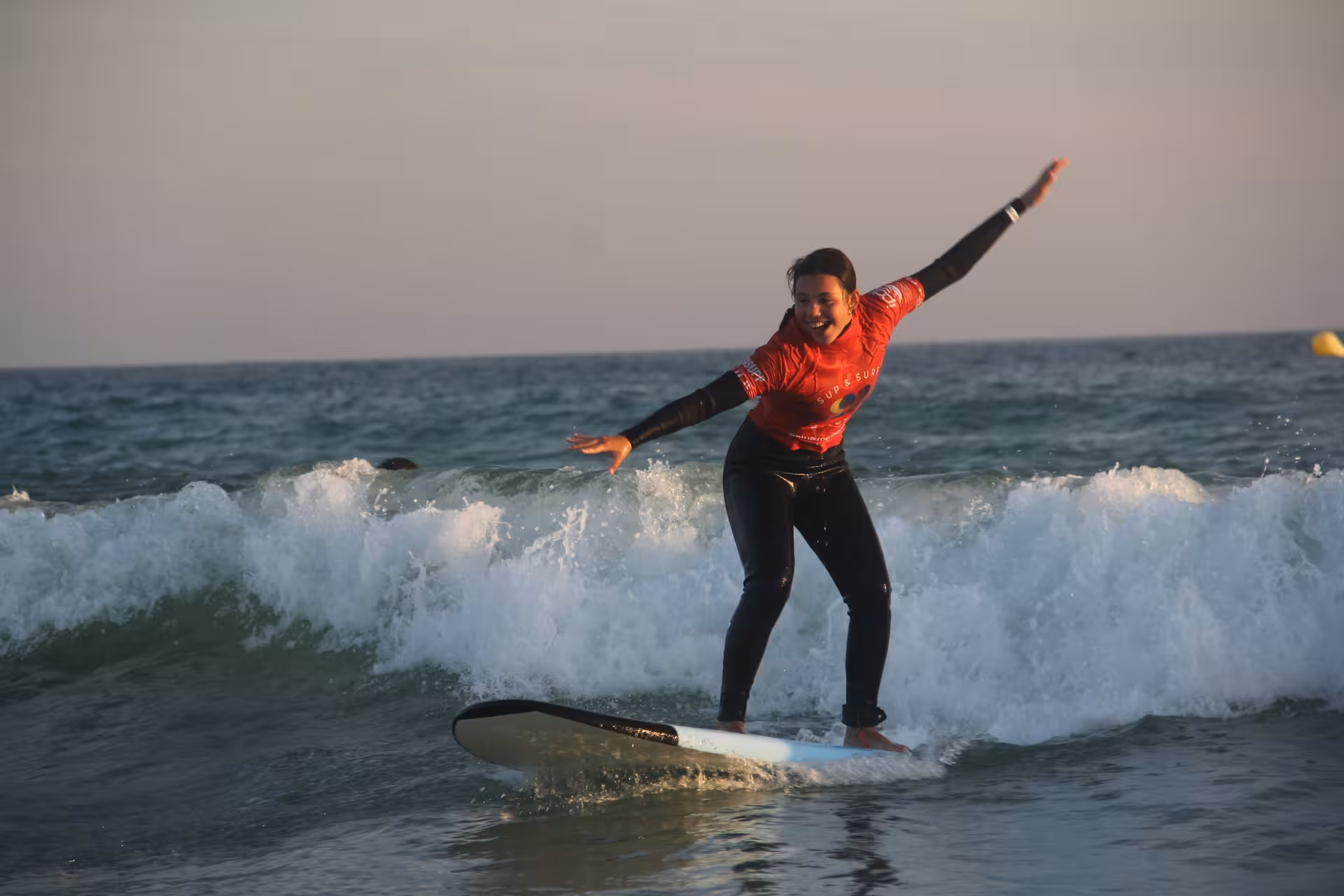Smiling beginner riding a wave on a softboard in a 3-hour group surf course, enjoying safe coaching in warm waters
