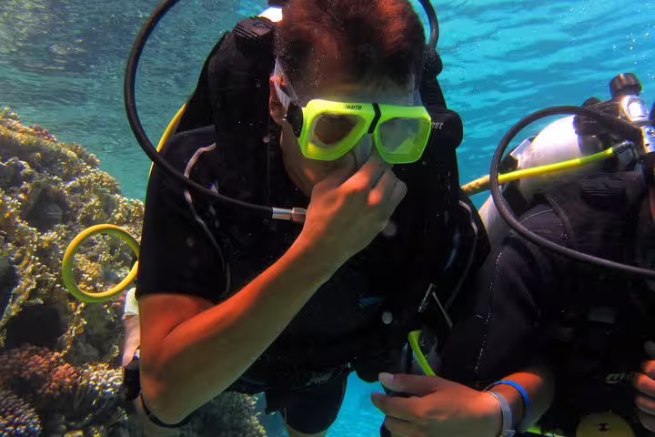 Beginner scuba diver adjusting mask beside coral reef on an intro diving and snorkeling day trip