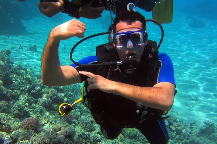 Beginner scuba diver posing above colorful coral reef on an intro diving and snorkeling day trip
