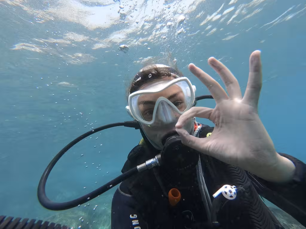Beginner scuba diver signaling OK underwater in clear blue sea, perfect for first-time diving enthusiasts.