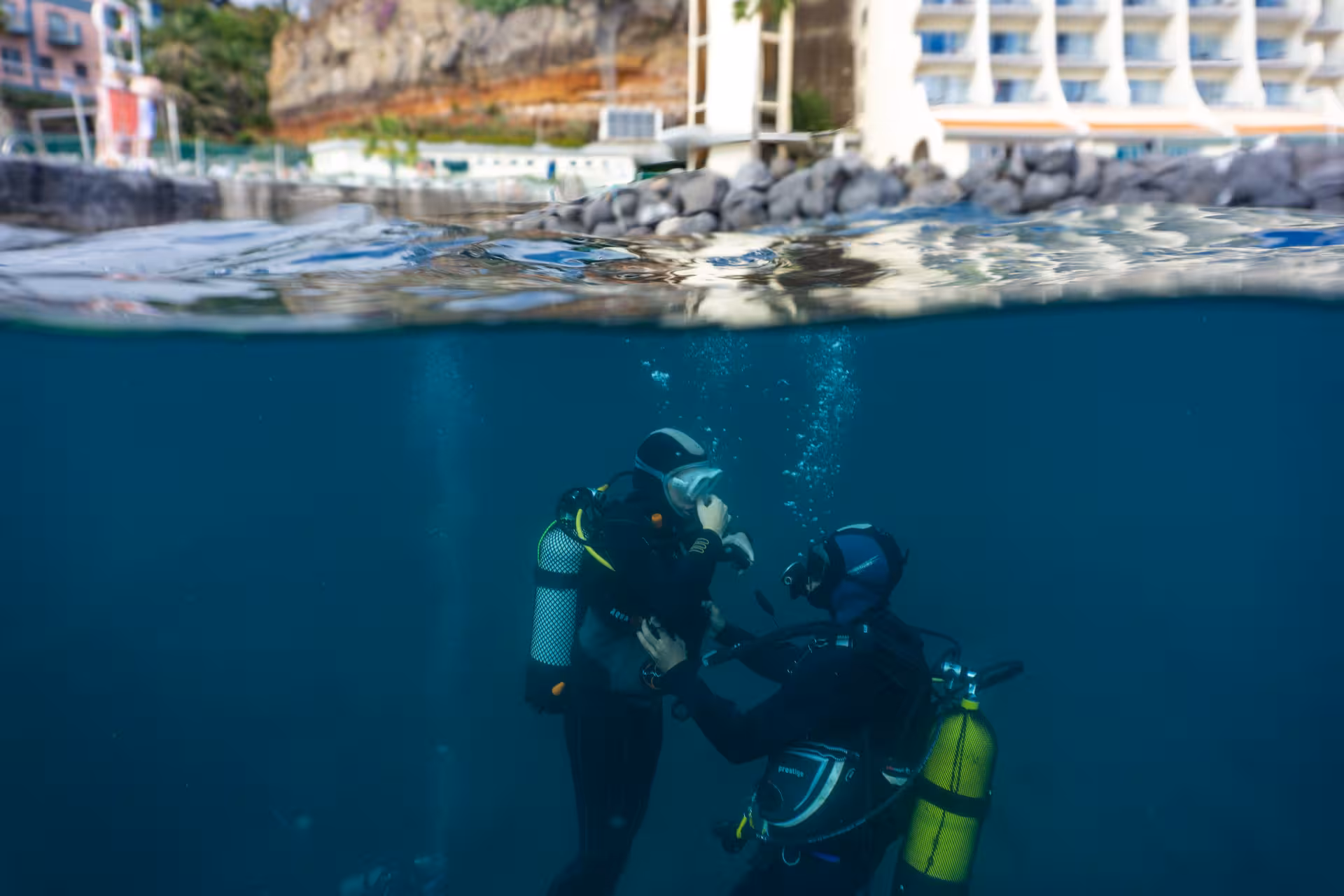 Two beginner divers receiving scuba training in clear waters near a coastal resort, perfect for a first-time experience.