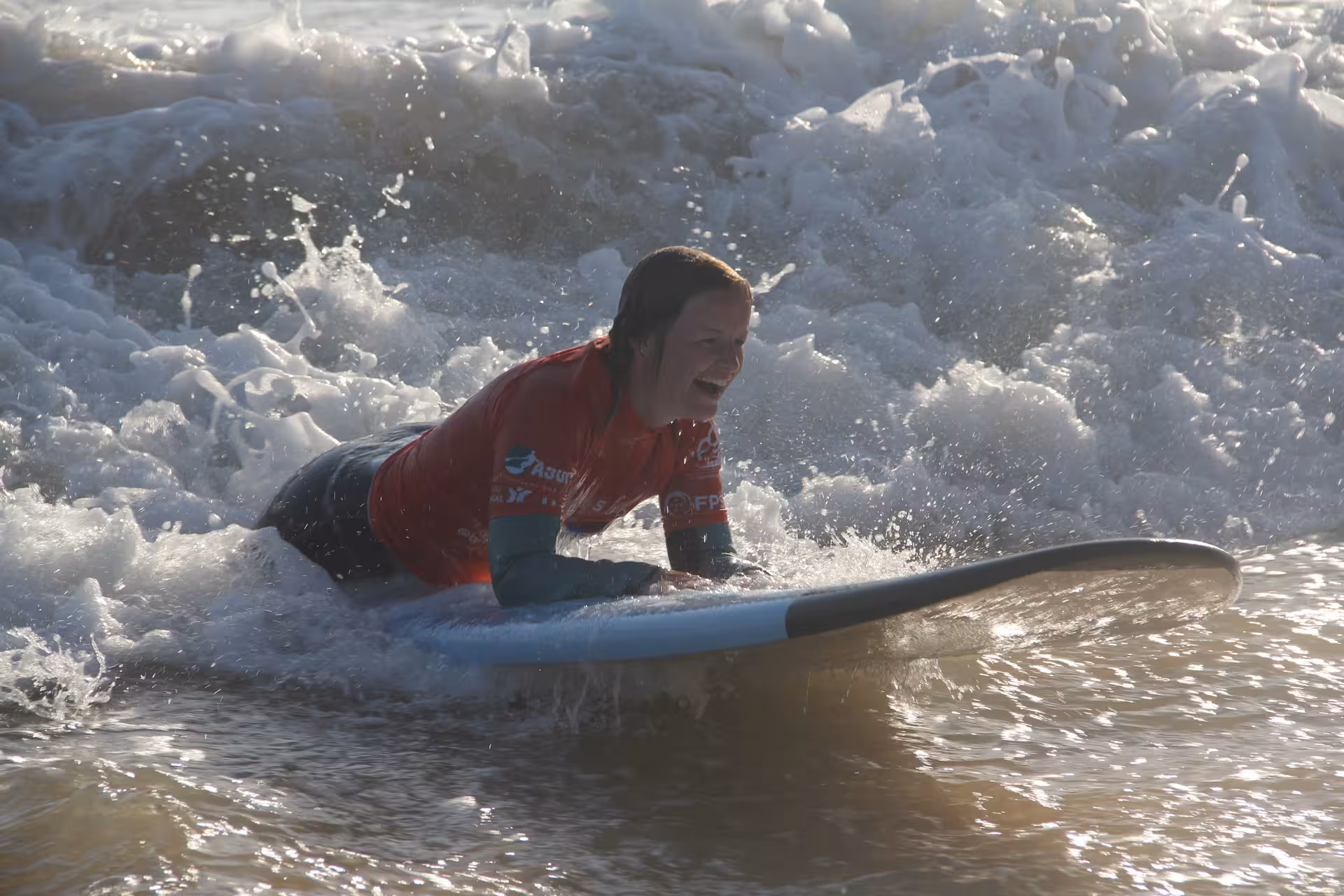 Beginner surfer laughing while riding a gentle wave on a foam surfboard during a 3-hour group surf lesson